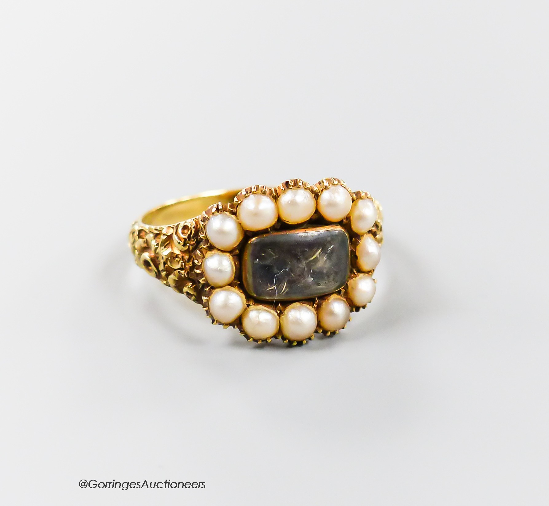A 19th century yellow metal and split pearl set mourning ring, with plaited hair beneath a glazed panel, size N/O, gross 4.5 grams.